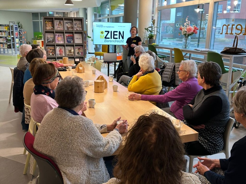 Groep aan tafel kijkend naar presentatie